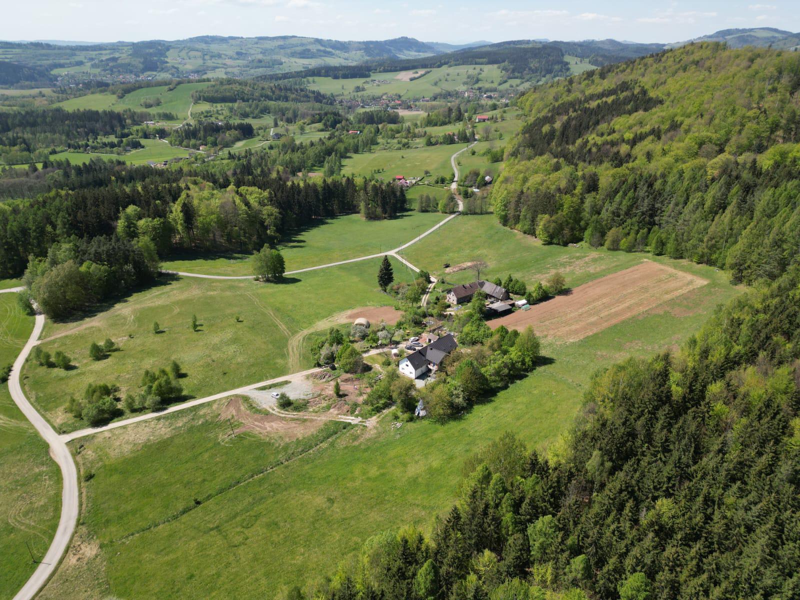 Panoramiczny widok z drona na dolinę, pola, lasy i rozrzucone zabudowania otoczone łagodnymi wzgórzami.